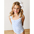 Young girl wearing a blue floral one-piece swimsuit with a white bow in her hair