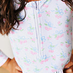 Close up of the top of a girl's two-piece zip front swimsuit in a pink cherries print.