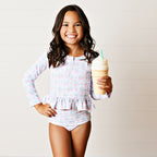 Young girl in a two-piece swimsuit with long-sleeve top and matching bottoms in a pink cherries print holding an ice cream cone.