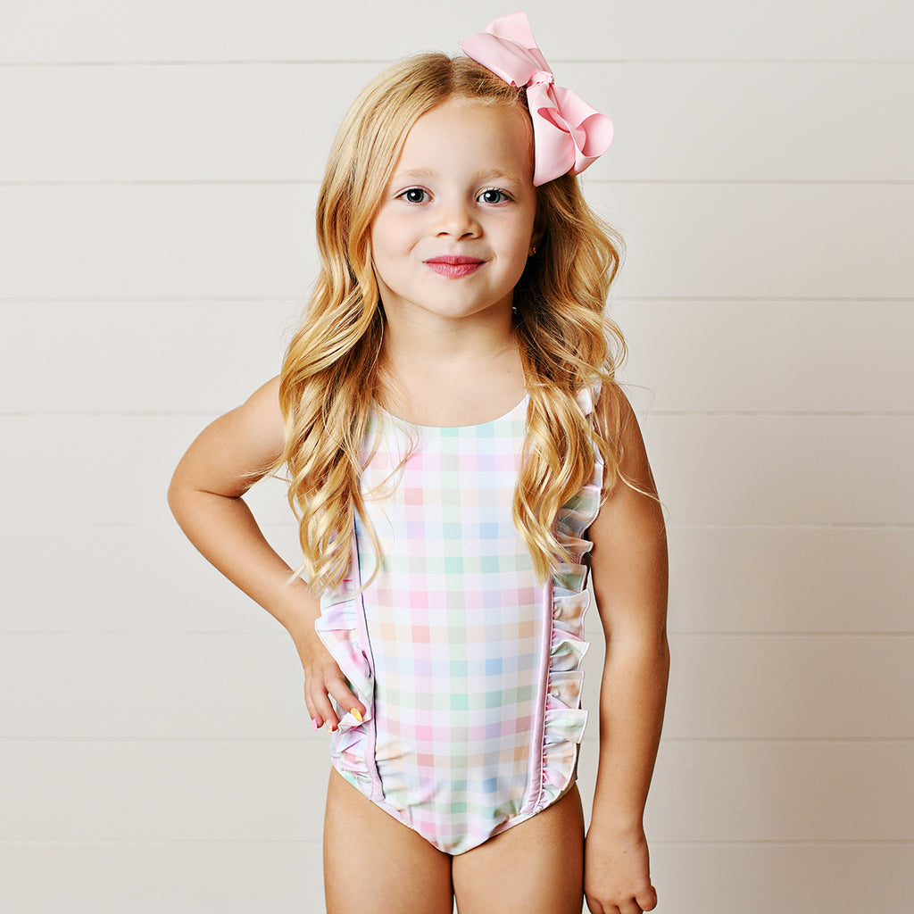 Young girl wearing a pastel plaid one-piece swimsuit with ruffled straps and a large pink bow