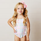 Young girl wearing a pastel plaid one-piece swimsuit with ruffled straps and a large pink bow