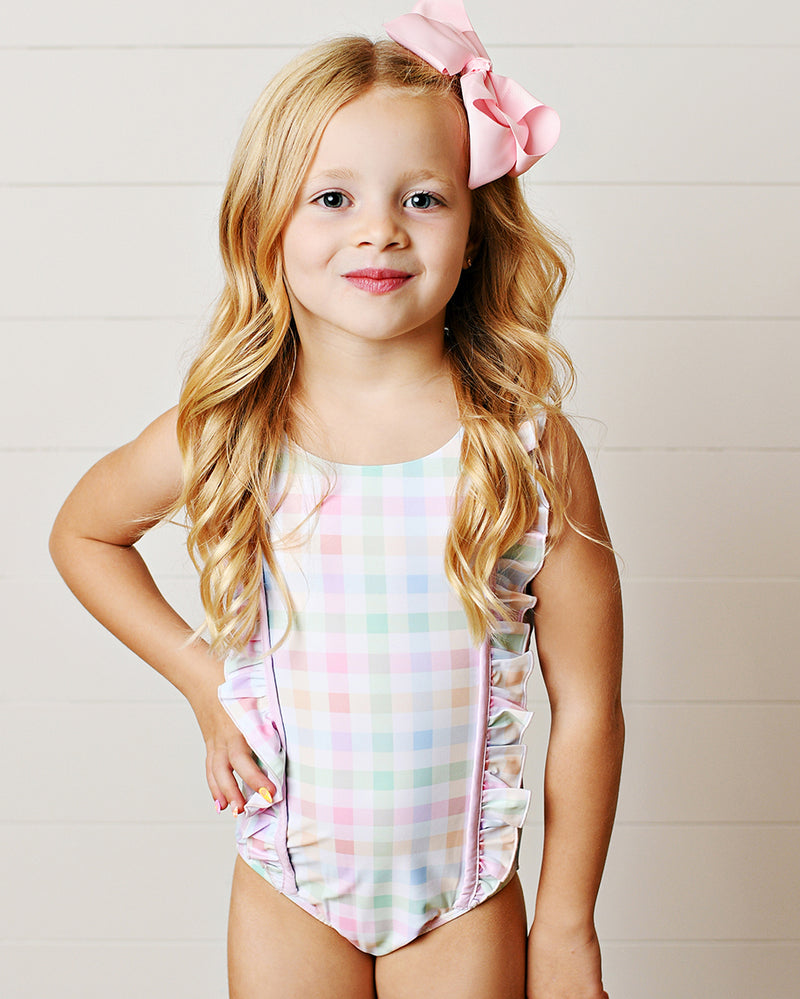 Young girl wearing a pastel gingham swimsuit with a pink bow in her hair