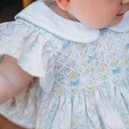 Close-up of a child wearing a smocked pastel floral dress with blue bows.