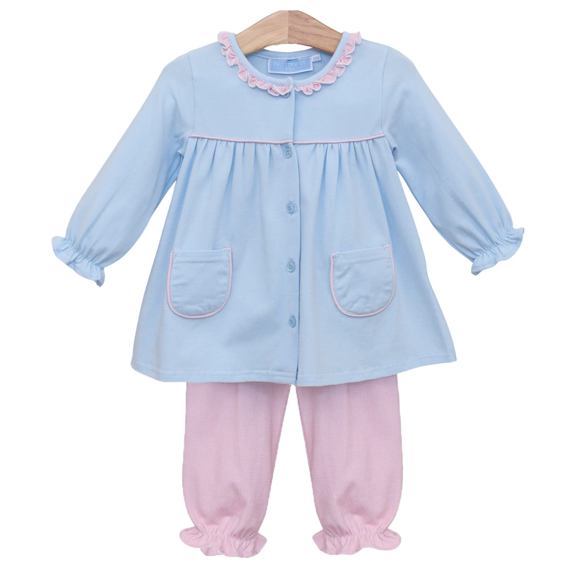 A toddler girl's two-piece outfit consisting of a light blue long-sleeve top with pink ruffle trim, buttons, and pocket edges, paired with light pink microcheck pants with ruffled cuffs.